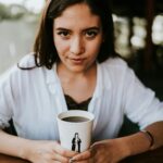 Portrait of a young woman holding a coffee cup indoors with a thoughtful expression.